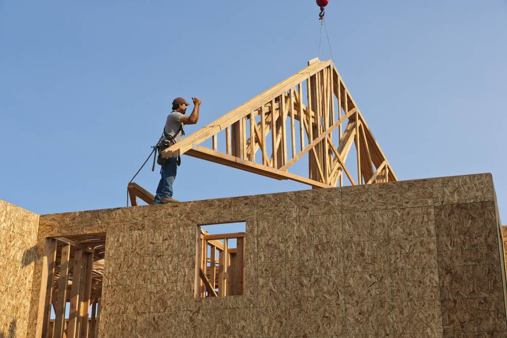 Montage eines Dachstuhls auf einem Holzrahmenbau – Zimmerer richtet Giebelkonstruktion per Kran ein.
