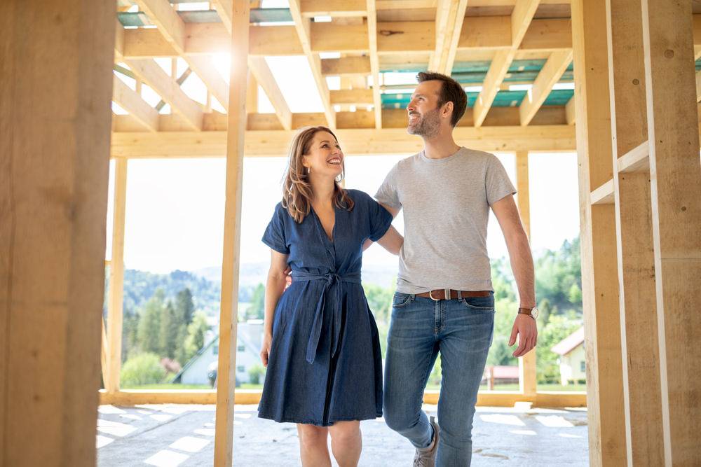 Glückliches Paar im Rohbau ihres Eigenheims in Holzrahmenbauweise – Hausbau mit der Zimmerei als Lebensprojekt.