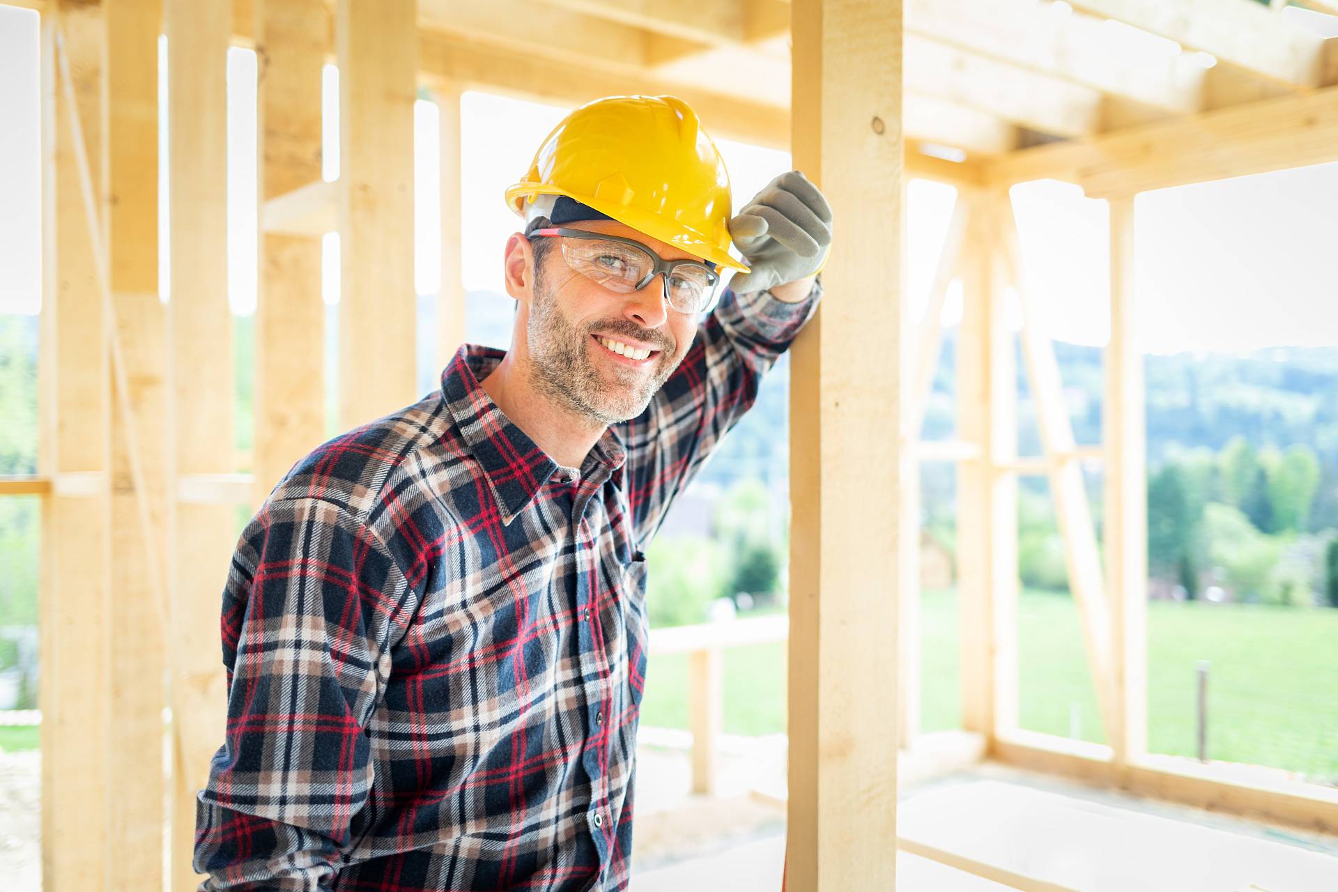 Zimmermann mit Schutzhelm und Arbeitskleidung auf Baustelle für Holzrahmenbau – lächelnd beim Rohbau eines Holzhauses.