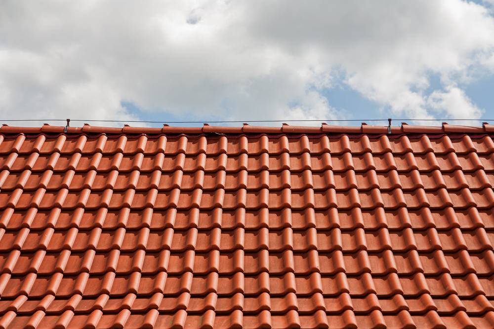 Neu gedecktes Ziegeldach mit roten Dachpfannen unter bewölktem Himmel
